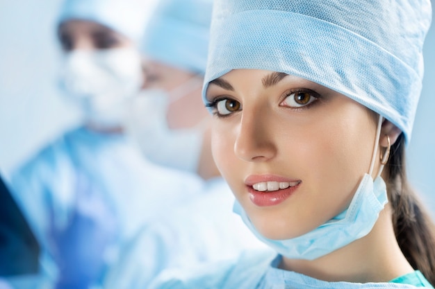 Портрет счастливой молодой женщины-хирурга или стажера после успешной операции со своими коллегами, работающими