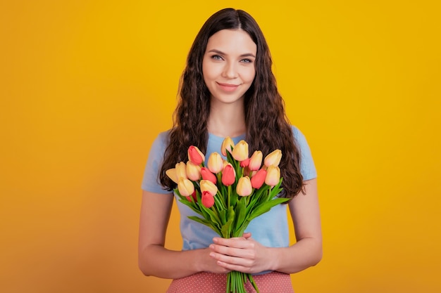 Portrait of a happy young girl in holding tulips bouquet present isolated over yellow color background
