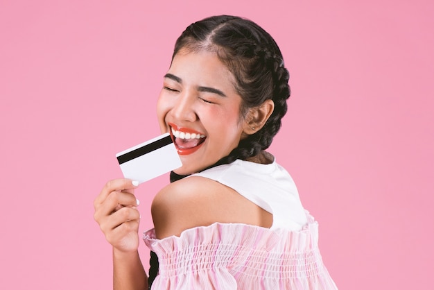 portrait of happy young girl showing credit card over pink background