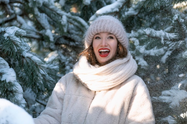 Portrait of happy young girl in winter outdoors near the snowcovered pine trees Sunny day