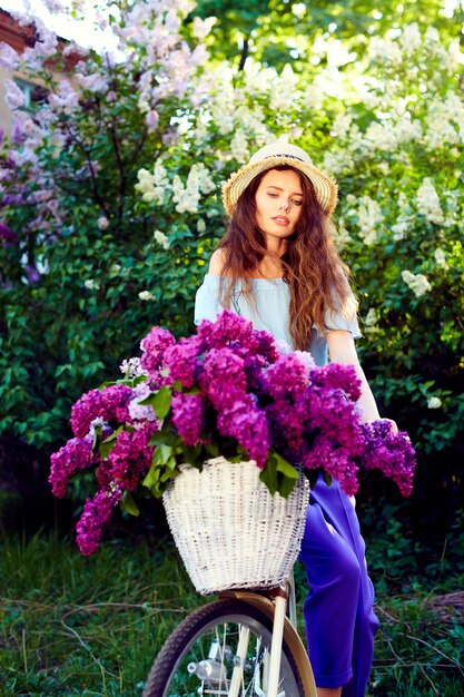 Portrait of a happy young girl with vintage bicycle and flowers on city background in the sunlight outdoor.