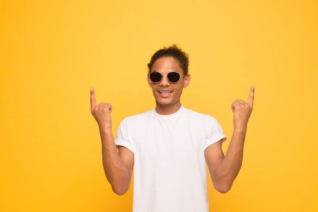 Portrait of happy young good-looking afro american man with in casual smiling in glasses, pointing up with finger,