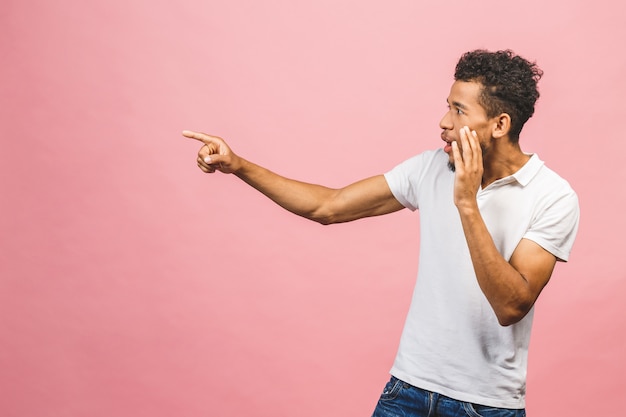 Ritratto di giovane bello studente maschio dalla pelle abbronzata felice con l'acconciatura afro nel sorridere casuale, indicando da parte con il dito, con l'espressione eccitata del fronte.