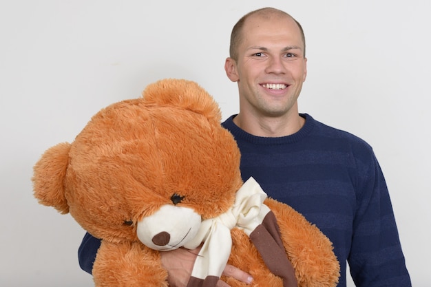 Portrait of happy young handsome bald man holding big teddy bear