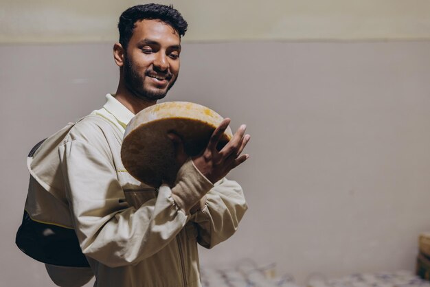 Photo portrait of happy young indian beekeeper holding wax and honey and working in beekeeping factory