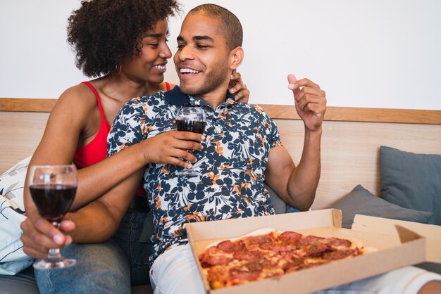 一緒に夕食を食べて、彼らの家でワインを飲む幸せな若いラテンカップルの肖像画。ライフスタイルと人間関係の概念。