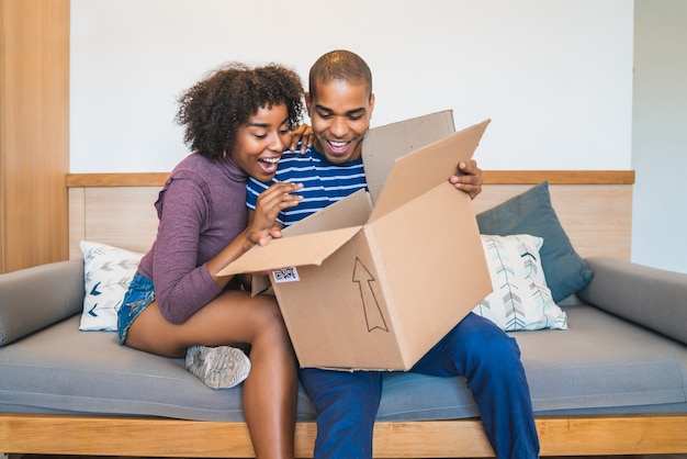 Portrait of happy young latin couple opening a package at home. Delivery, shipping and postal service concept.