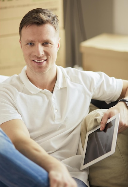 Portrait of happy young man moving in new home Man holding digital tablet in his arms