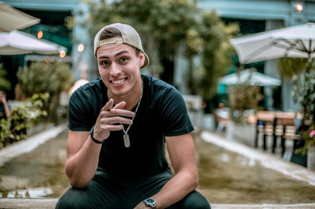 Photo portrait of happy young man pointing while sitting outdoors