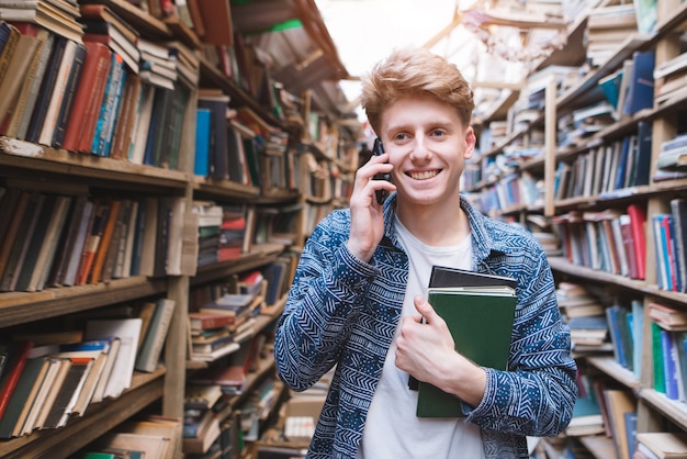 Portrait of a happy young man standing with books in his hands in a public library