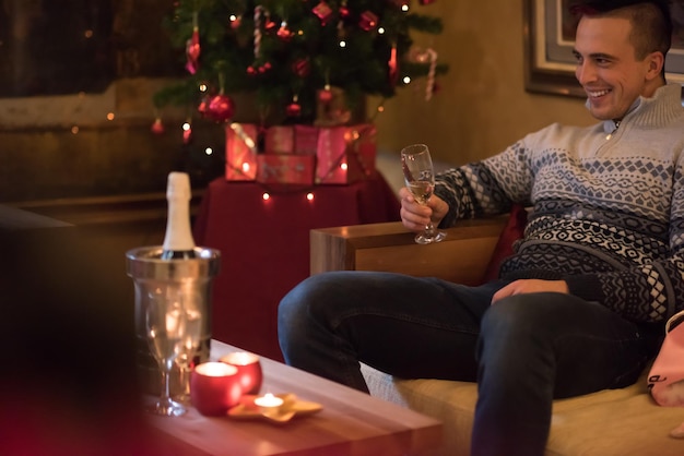 Portrait of a happy young man with a glass of champagne celebrating winter holidays at home beautifully decorated for Christmas