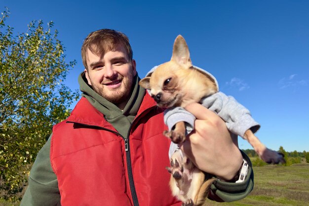 Portrait of happy young man with his chihuahua dog hold on hands little puppy on natural background