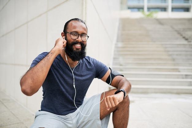 Portrait of happy young mixed race man with beard putting earphones into ears outdoors