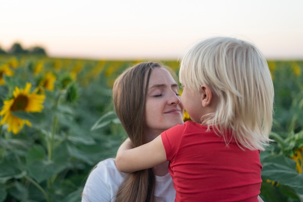 Portrait of happy young mother and little son on field of sunflowers surface. Tenderness and trust.