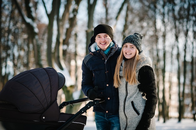 Portrait of a happy young parents stand with a stroller and baby in a winter park. Family concept.