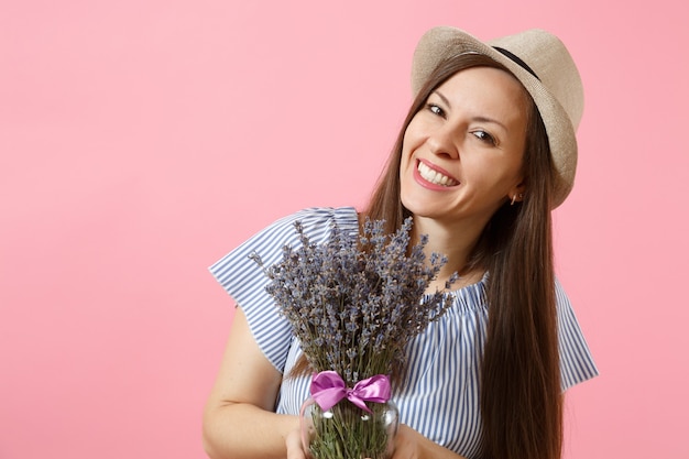 青いドレス、明るいトレンドのピンクの背景に分離された美しい紫色のラベンダーの花の花束を保持している帽子の幸せな若い優しい女性の肖像画。国際女性の日の休日の概念。