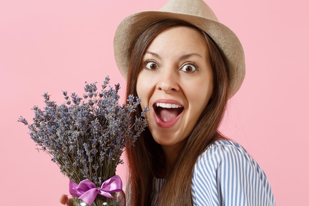 Portrait of a happy young tender woman in blue dress, hat holding bouquet of beautiful purple lavender flowers isolated on bright trending pink background. International Women's Day holiday concept.