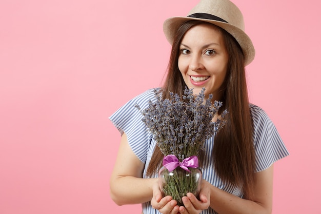 明るいトレンドのピンクの背景に分離された美しい紫色のラベンダーの花の花束を保持している青いドレス麦わら帽子の幸せな若い優しい女性の肖像画。国際女性の日の休日の概念