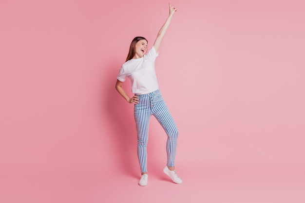 Portrait of a happy young woman dancing raise hand direct finger up