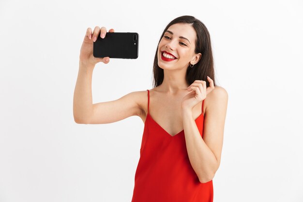 携帯電話でselfieを撮って、孤立したドレスで幸せな若い女性の肖像画