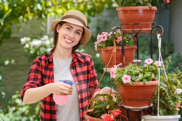 Portrait of happy young woman gardener spraying water on plants