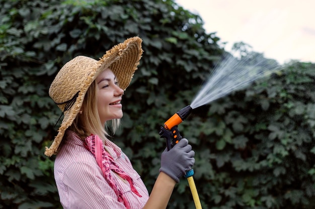 ホース趣味の概念を持つ庭に水をまく幸せな若い女性の庭師の肖像画