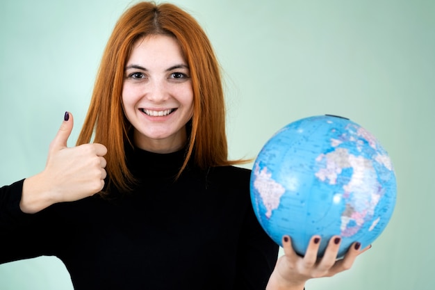 Portrait of a happy young woman holding geographic globe of the world in her hands. Travel destination and planet protection concept.