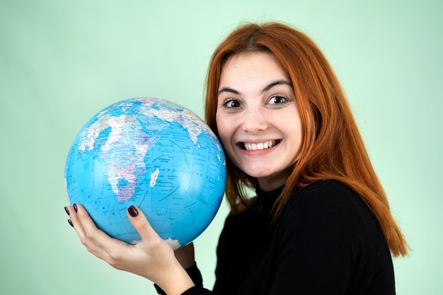 Portrait of a happy young woman holding geographic globe of the world in her hands. Travel destination and planet protection concept.