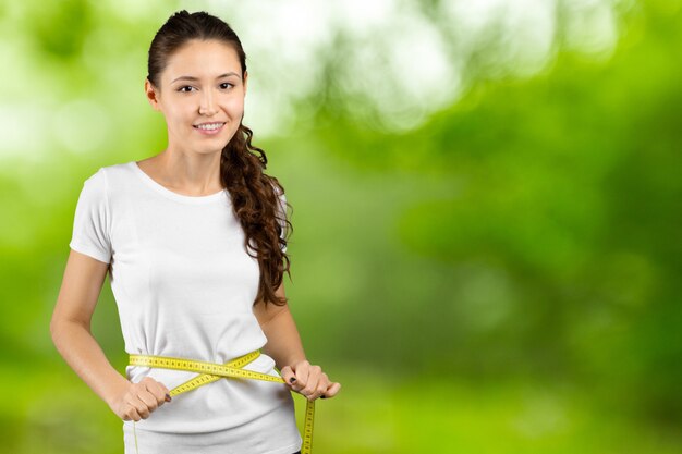 Portrait of a happy young  woman holding measuring tape around her waist