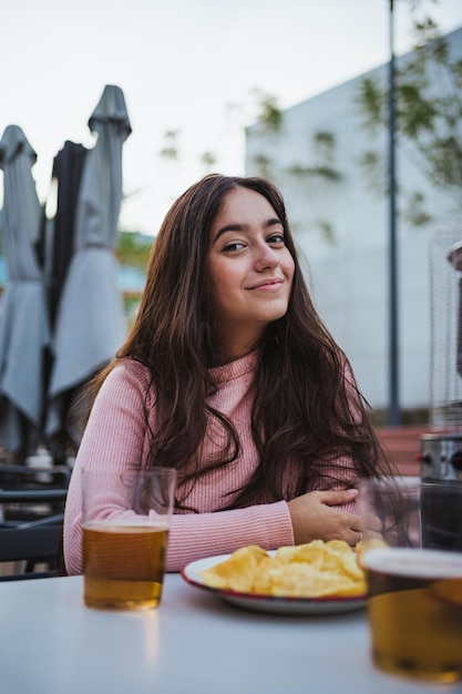 Портрет счастливой молодой женщины, смотрящей в камеру, пока она сидит в баре на открытом воздухе