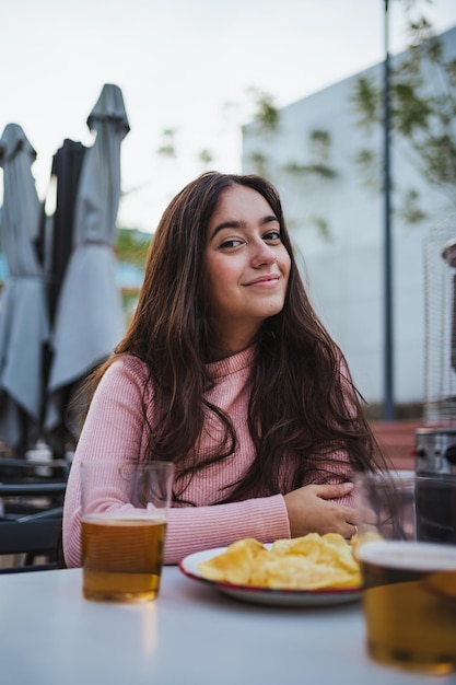 彼女は屋外のバーに座っている間、カメラを見て幸せな若い女性の肖像画