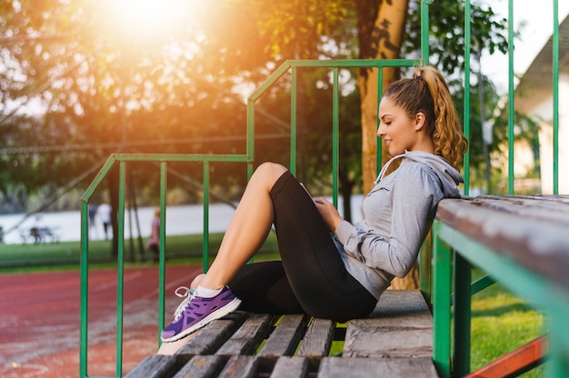 Portrait of happy young woman sitting outside on bench reading a text message on her mobile phone