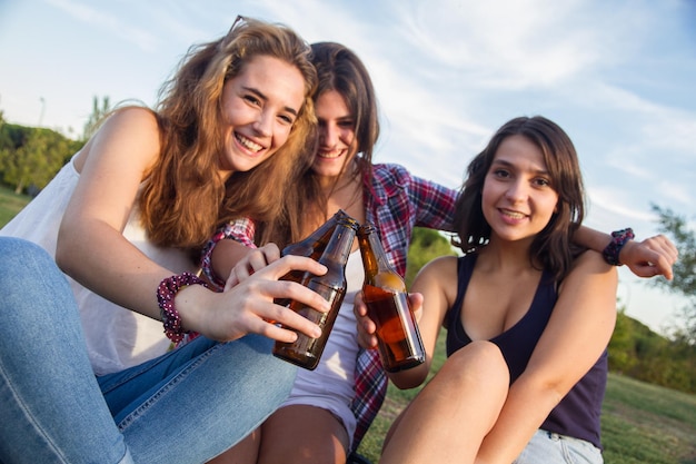 Photo portrait of happy young woman toasting beer bottle with female friends on field