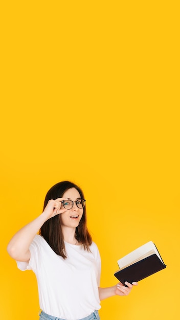 Portrait of a happy young woman wearing glasses and white Tshirt immersed in reading a book with a