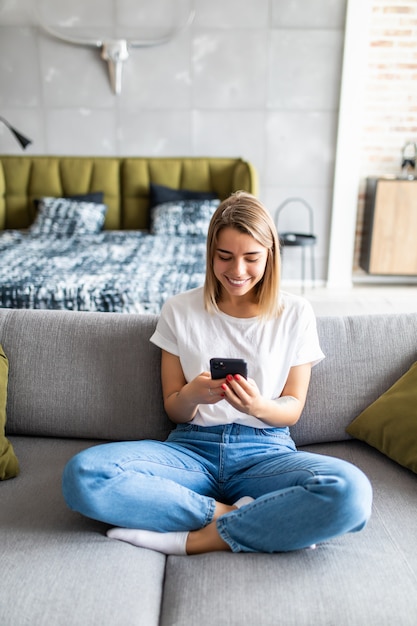 自宅のソファに座って携帯電話を持つ幸せな若い女性の肖像画