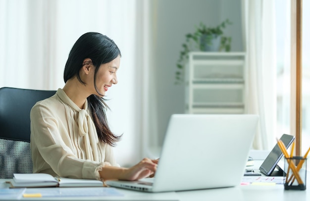 Portrait of happy young woman working on tablet pc while sitting at her working place in office