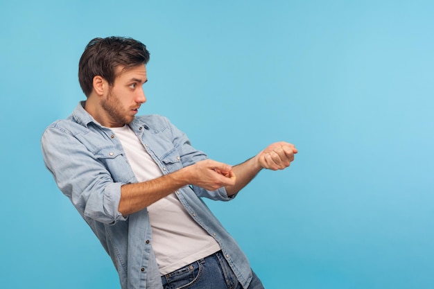 Ritratto di un uomo laborioso e persistente in camicia di jeans da lavoratore che tira la corda virtuale, imitando per tenere oggetti pesanti, lottando e facendo un grande sforzo. tiro in studio indoor isolato su sfondo blu