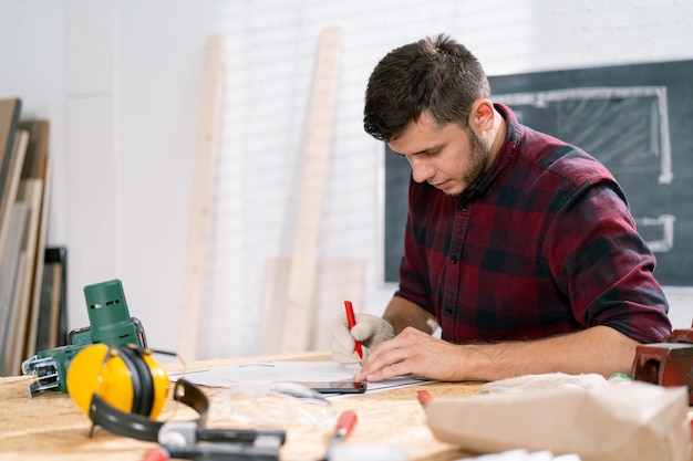 portrait of a hardworking professional carpenter holding a angular ruler and pencil while measuring