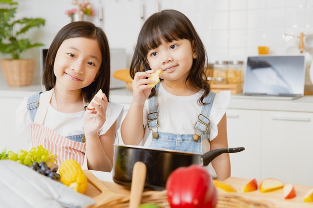 リンゴの果実を食べてキッチンで一緒に遊んで幸せな肖像画の健康な女の子の子供たち