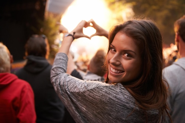 Портрет сердца и жеста руки с женщиной на концерте в составе толпы или публики фестиваля Лицо на вечеринке и улыбка со счастливой молодой женщиной на открытом воздухе на музыкальном представлении