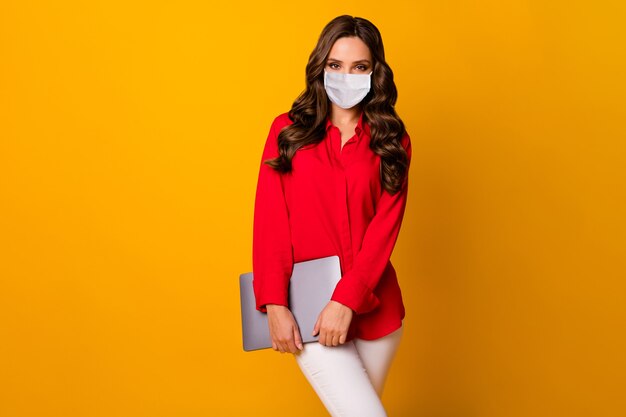 Portrait of her she attractive gorgeous wavy-haired girl wearing safety mask carrying laptop keep social distance stop pandemia isolated bright vivid shine vibrant yellow color background