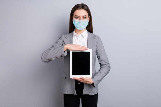 Portrait of her she attractive lady wearing safety mask holding in hands tablet stop pandemia mers cov influenza disease wfh anti crisis economy remote distance isolated grey color background