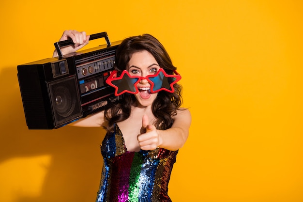 Photo portrait of her she-looking attractive cheerful cheery wavy-haired girl wearing cool specs carrying boombox choosing you having fun isolated bright vivid shine vibrant yellow color background