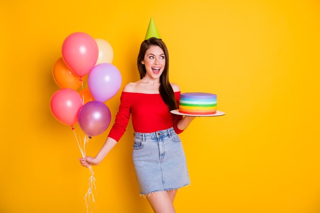 Portrait of her she nice attractive pretty cheerful cheery girl holding in hand homemade cake helium balls having fun event festive isolated bright vivid shine vibrant yellow color background