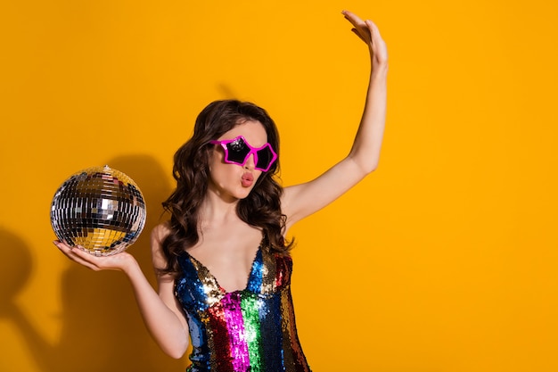 Photo portrait of her she nice attractive pretty lovely cool wavy-haired girl holding in hand silver ball dancing having fun swag pout lips isolated bright vivid shine vibrant yellow color background