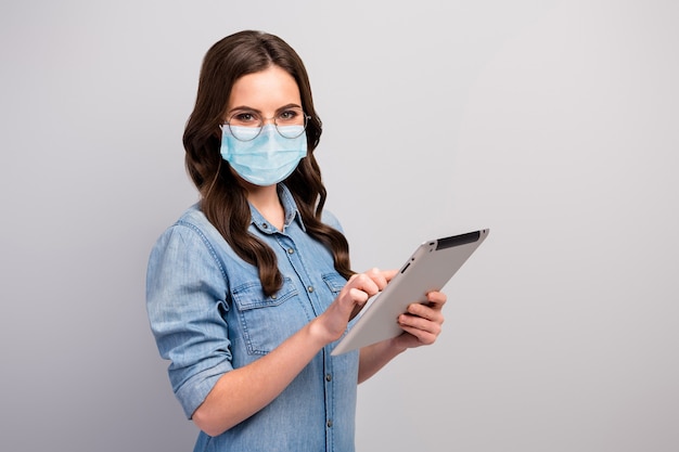 Portrait of her she nice attractive smart clever wavy-haired girl wearing gauze safety mask using device read disease influenza pandemia news medicine vaccine healthcare isolated gray color background