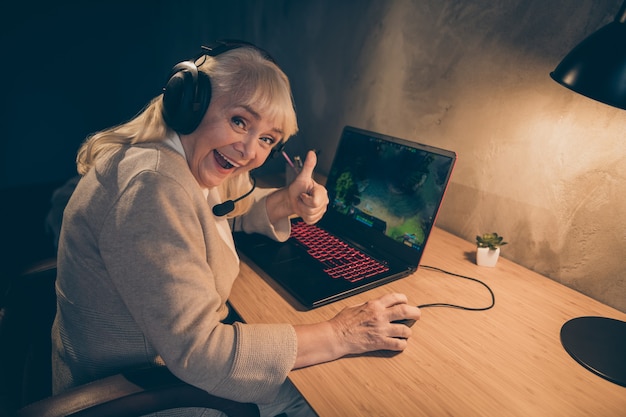 Portrait of her she nice cheerful cheery gray-haired blonde grandma playing game showing thumbup advice contest battle championship win at industrial loft modern concrete style interior