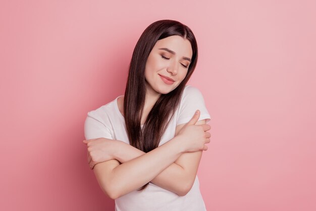 Portrait of her she nice cute sweet winsome lovely attractive charming cheerful girl hugging herself isolated over pink pastel background