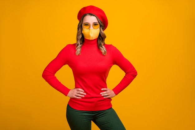 Portrait of her she nice-looking attractive charming pretty fashionable cheerful wavy-haired girl hands on hips wear medical mask isolated vivid yellow color background