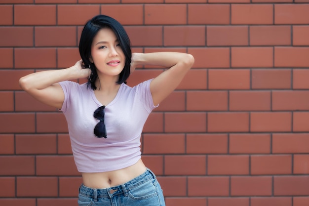 Портрет хипстерской девушки на фоне кирпичной стеныКрасивая азиатская женщина позирует для фото